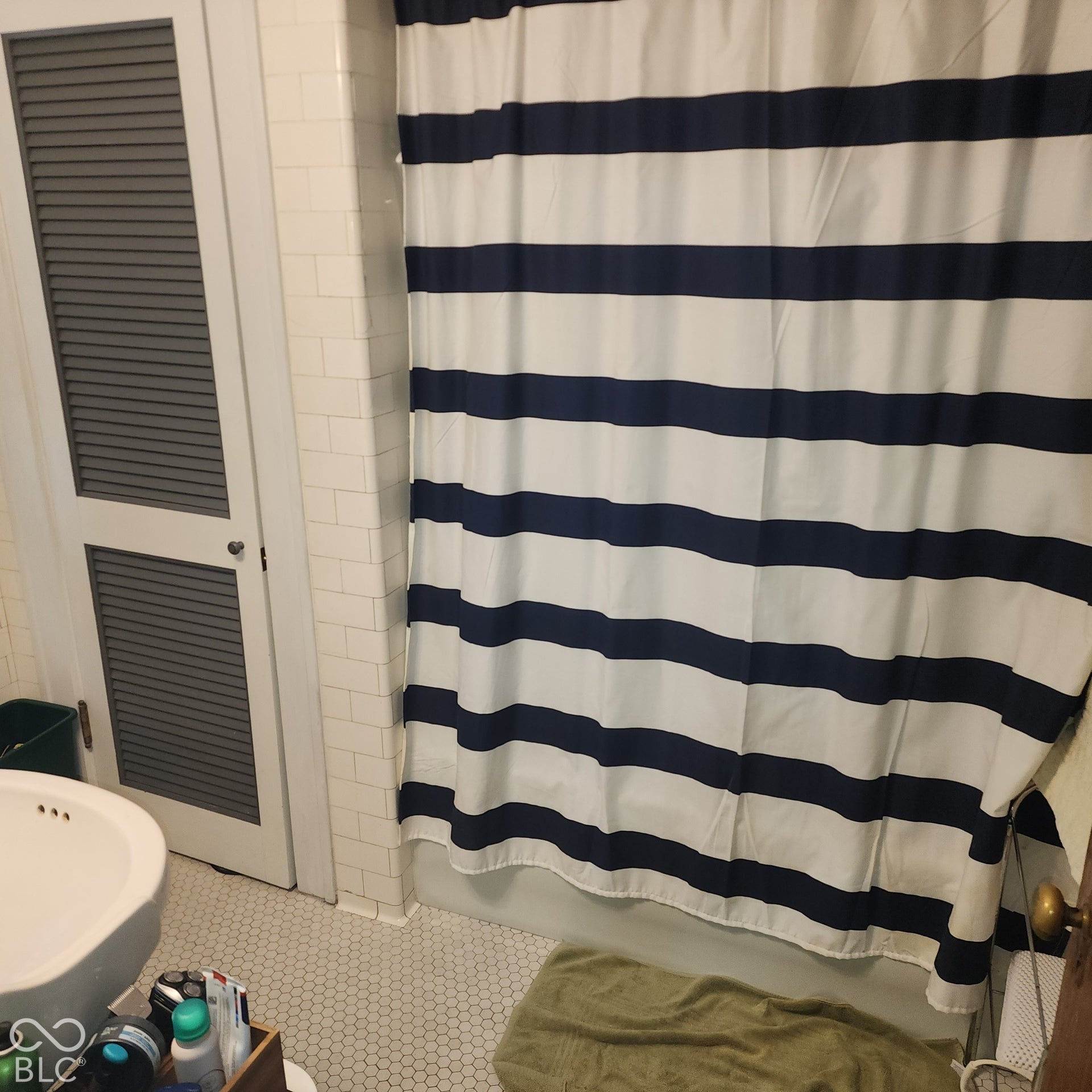 White hexagonal tile flooring, white subway tile wall, white bidet, and white louvered door
