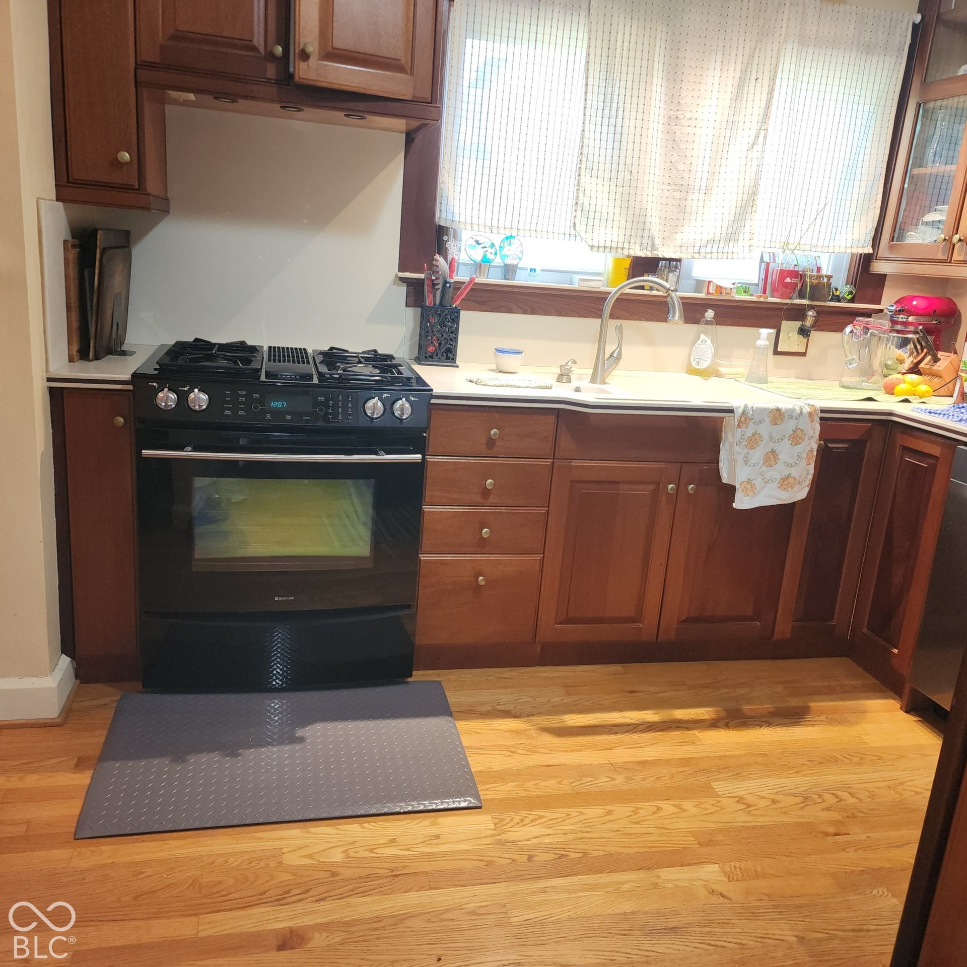 Wood-finish flooring, wood cabinetry, and a black range with an integrated cooktop
