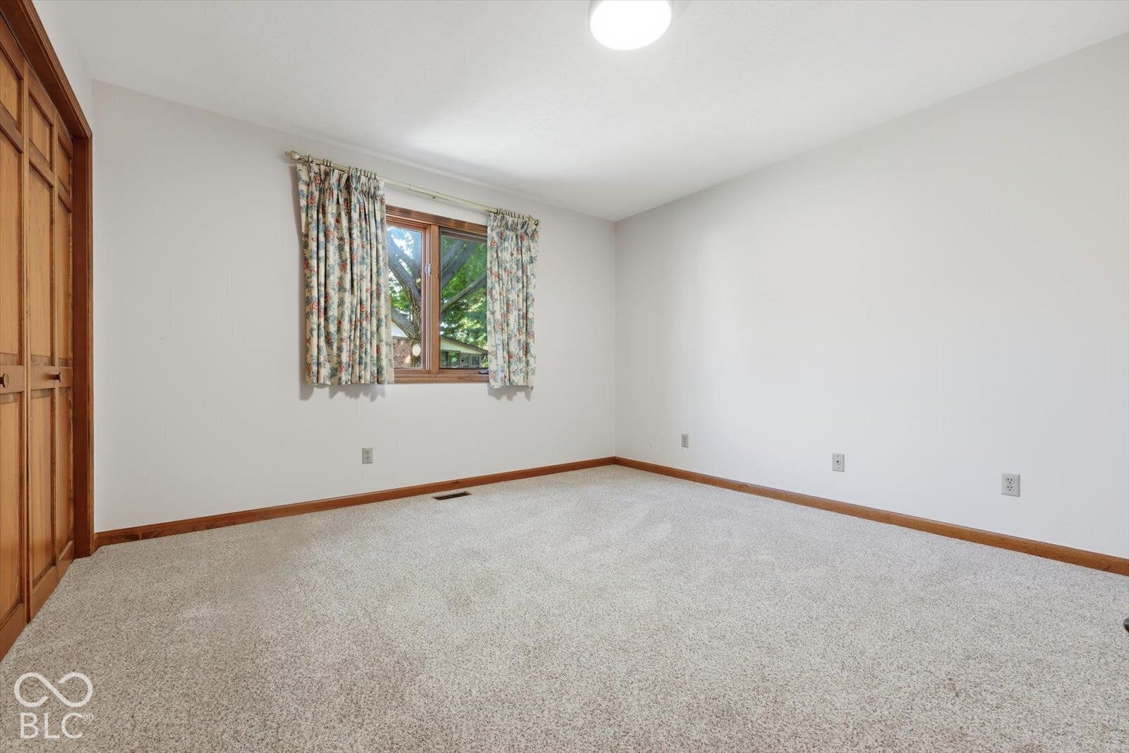 Bedroom Two-Neutral-toned carpeted room featuring a double-door wood-finish closet, wood-framed window, and ceiling-mounted light fixture