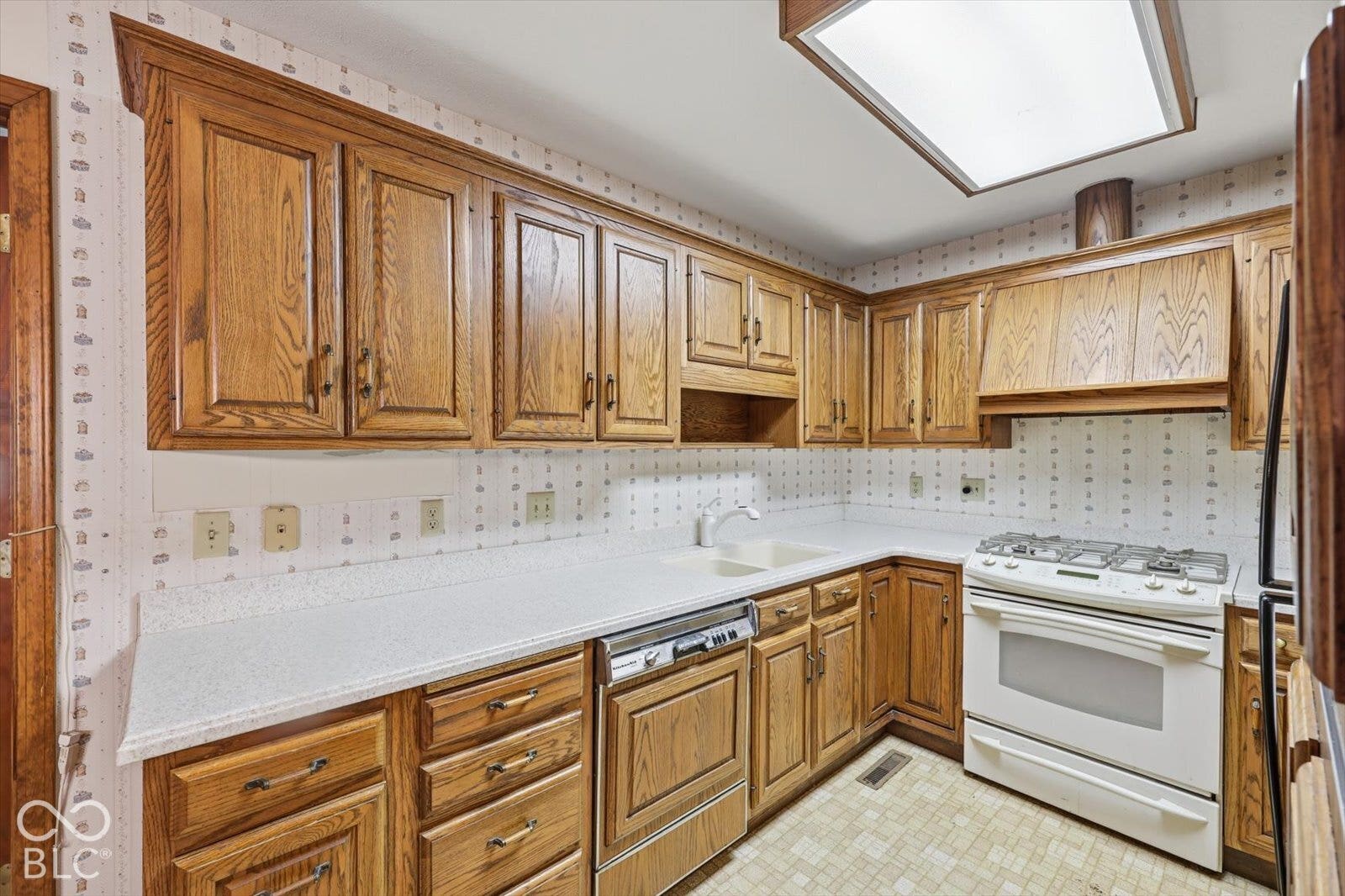 Virtually Altered - Kitchen featuring wood cabinetry, corian countertops, dual-basin sink, gas range, and recessed ceiling lighting