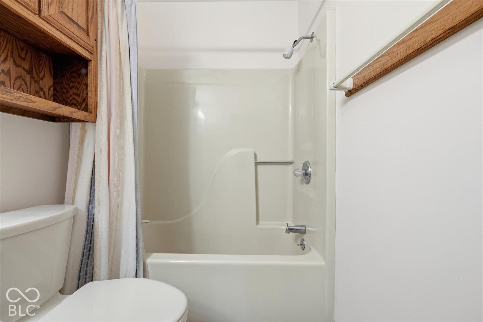Hall Full Bath featuring an acrylic tub and shower combination, wall-mounted wood cabinetry, and a chrome-finish shower fixture with integrated shelving