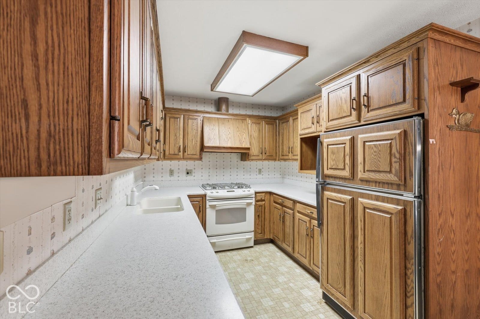 Virtually Altered - Kitchen featuring wood cabinetry, corian countertops, a white gas range, and a drop-in sink