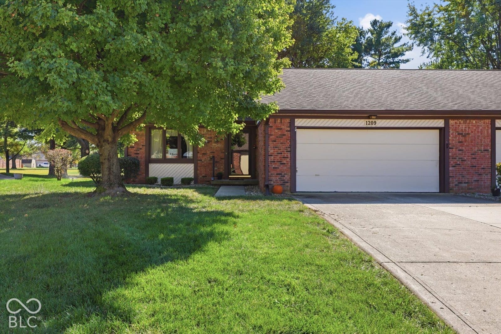 Brick exterior facade with an attached two-car garage, concrete driveway, and mature landscaping