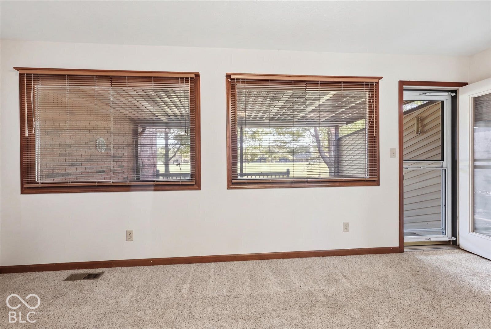 Virtually Altered - Sun Room- virtually staged as empty,  featuring dual windows with wood trim, neutral carpeting, and an exterior door with an integrated screen