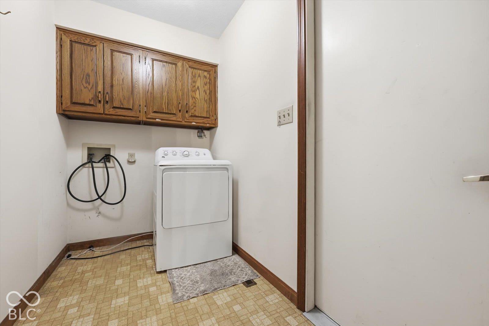 Laundry area featuring wood-finish wall-mounted cabinetry and patterned vinyl tile flooring