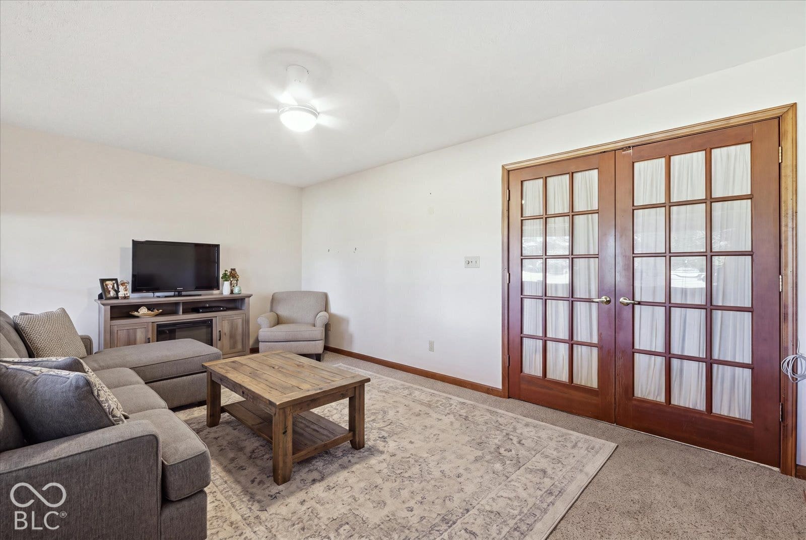 Virtually Altered - Sun Room- virtually staged furniture. Double French doors with wood trim and glass panes, ceiling-mounted light fixture, and neutral carpeted flooring