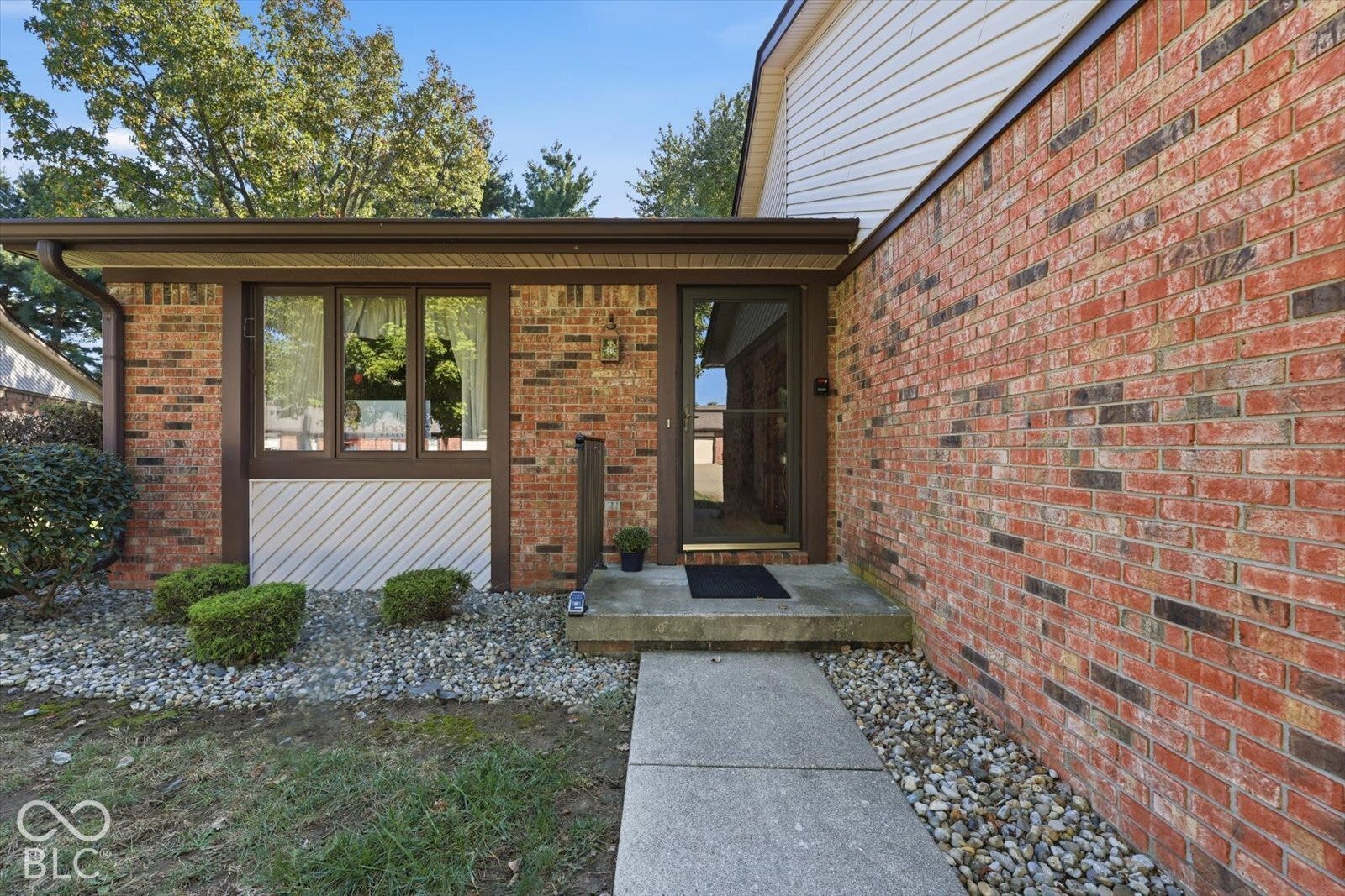Exterior facade featuring red brick masonry, white siding, a covered entryway, and stone landscaping