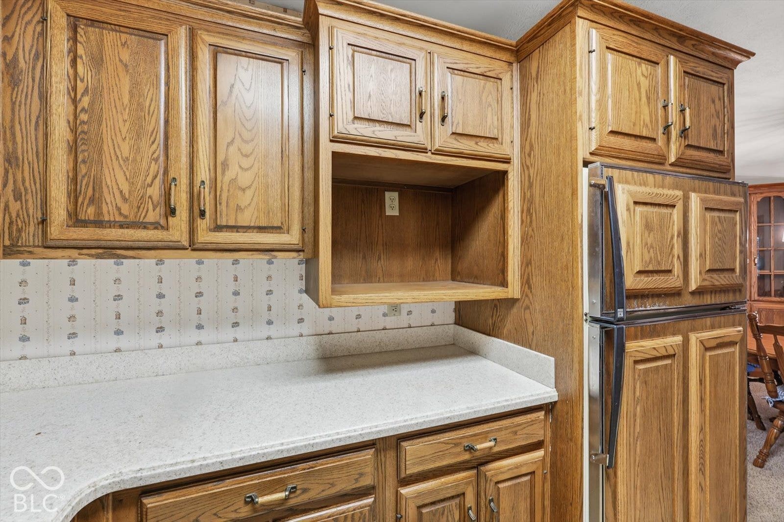 Virtually Altered - Kitchen featuring oak-finish cabinetry, corian countertops, built-in cabinetry over-counter storage, and an integrated refrigerator enclosure