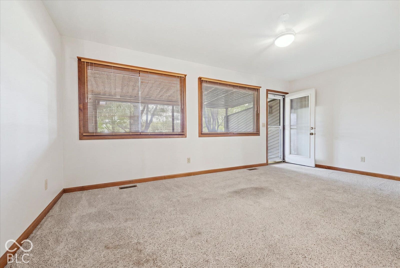 Virtually Altered - Sun Room with Heat & AC- featuring neutral carpeting, white walls, dual large windows with wood-tone trim, and a glass-paneled exterior door