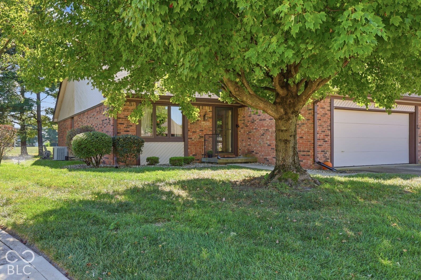 Virtually Altered - Single-story brick exterior featuring a multi-pane glass entry door, attached two-car garage, and mature tree landscaping