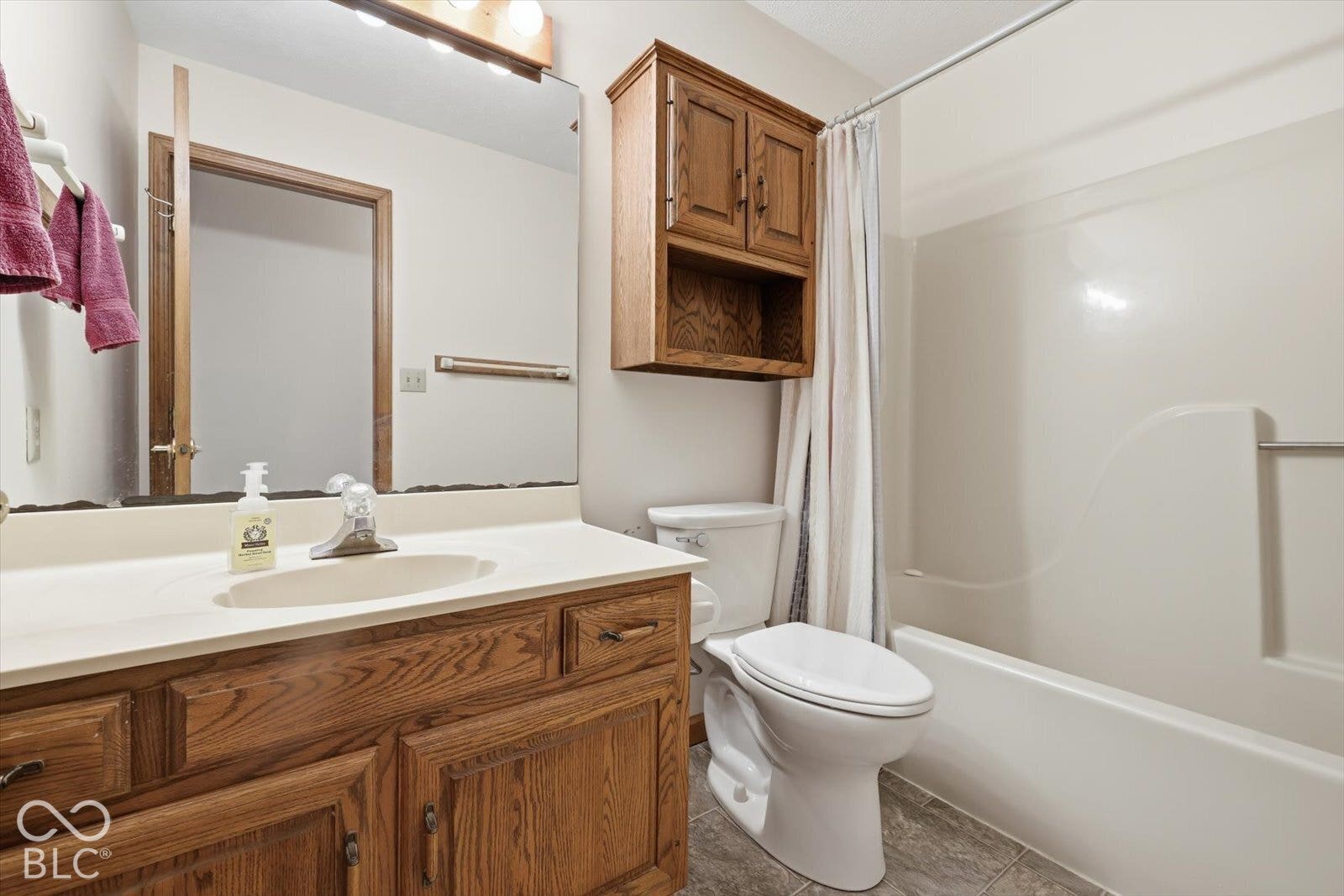 Hall Full Bath featuring a wood-finish vanity with an integrated sink, wall-mounted wood cabinetry, a full-width vanity mirror, and a combination tub and shower enclosure .