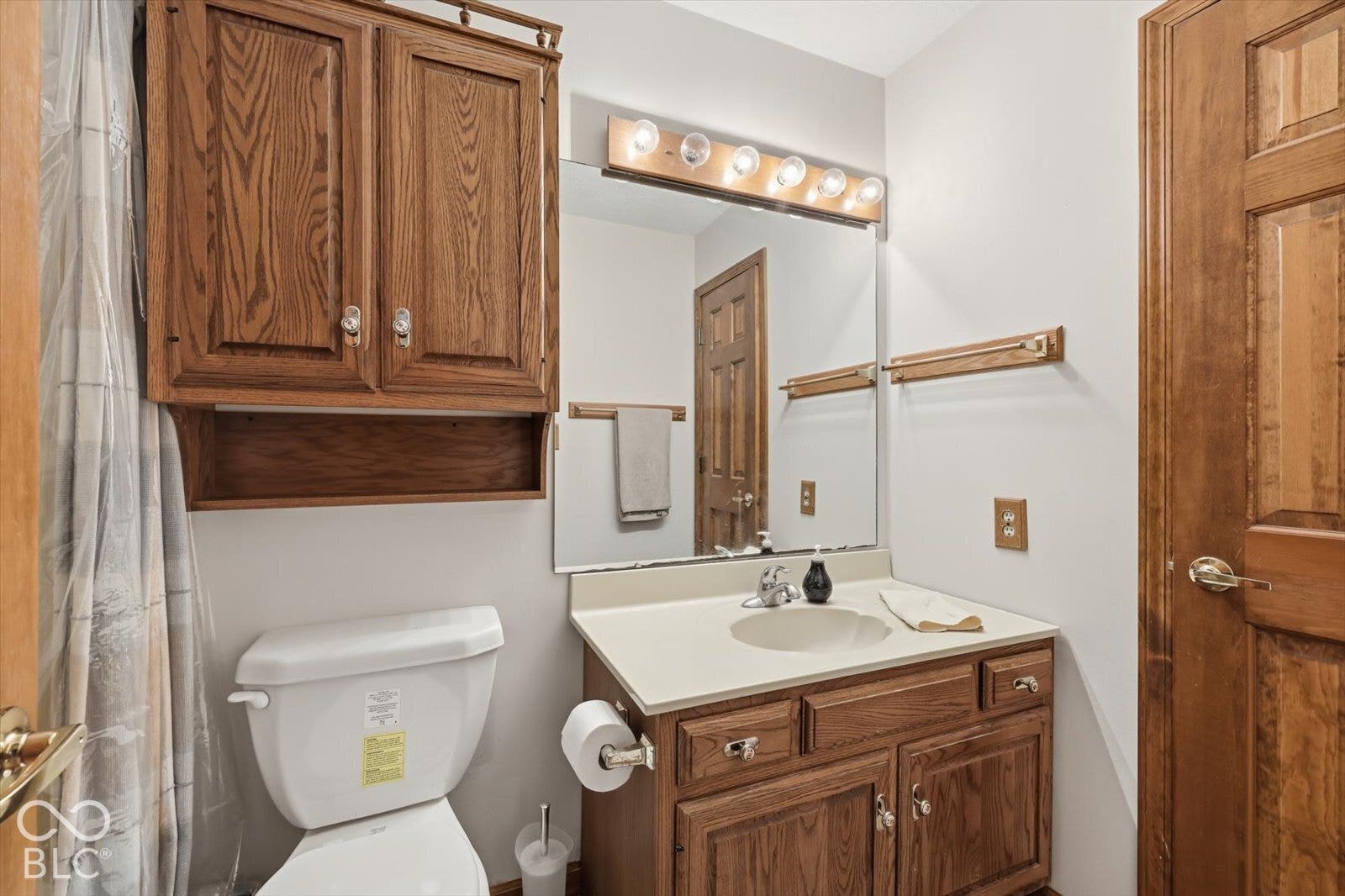Bathroom featuring a wood-finish vanity with a solid-surface countertop, an integrated sink basin, a large wall-mounted mirror with multi-bulb overhead lighting, and built-in wood-finish cabinetry, shower /tub in full bath.