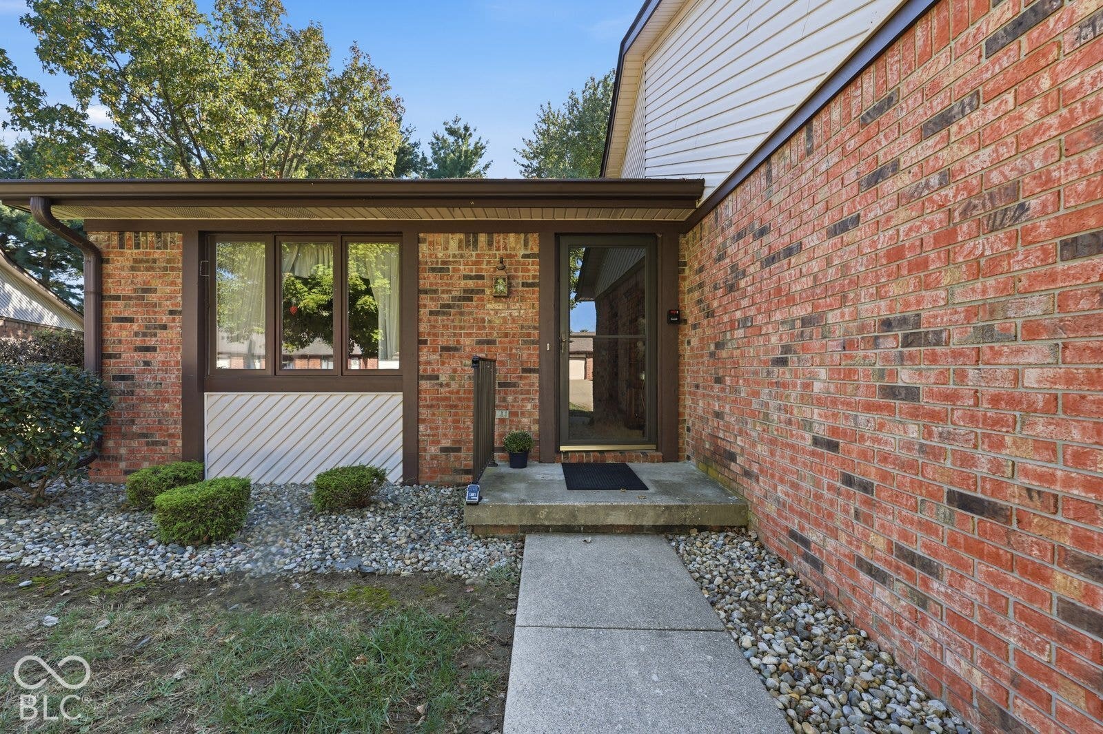Virtually Altered - Exterior entrance featuring red brick masonry, a multi-pane window with diagonal siding accents, a covered porch, and a concrete walkway