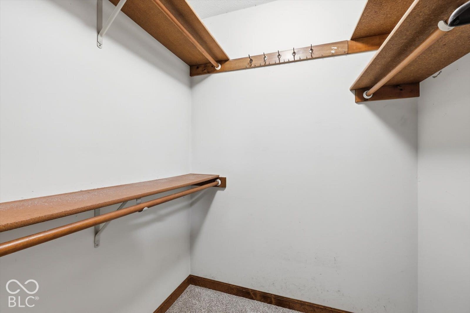 Primary Bedroom walk in closet-Storage closet featuring multi-level wooden shelving, integrated hanging rods, and a wall-mounted hook rack