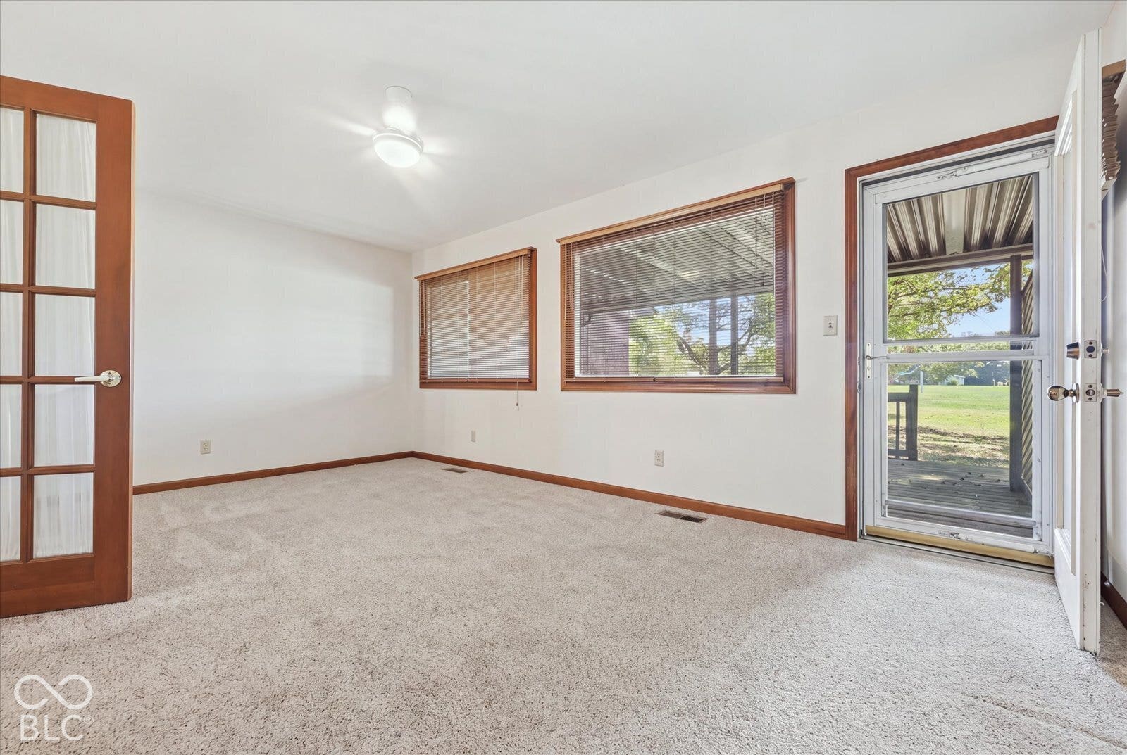 Virtually Altered - Sun Room carpeting, wood-trimmed windows, a glass-panel French door, and a exterior storm door with direct outdoor access