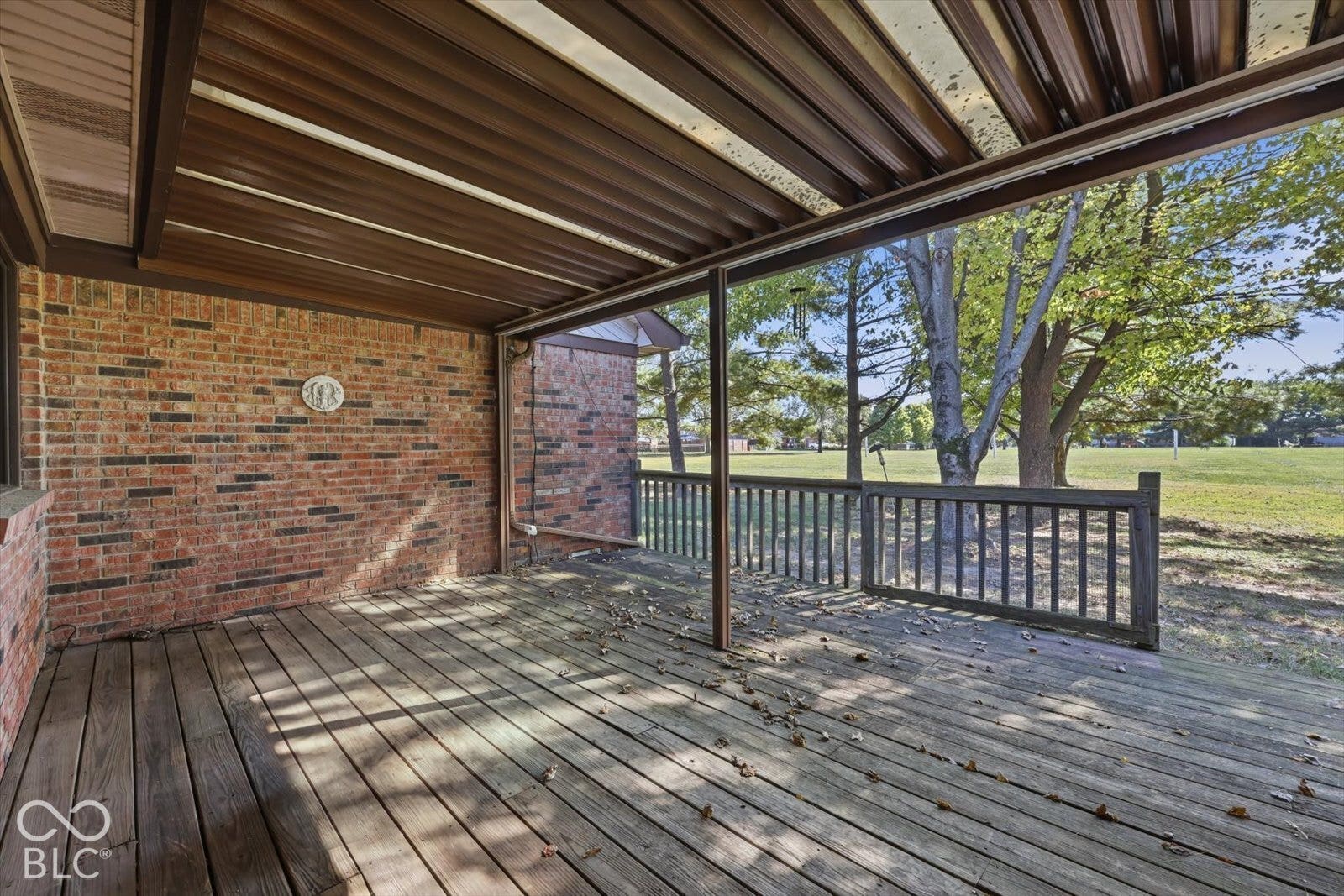 Virtually Altered - Covered porch featuring a wood-plank deck, brick exterior wall, and wood-slat railing