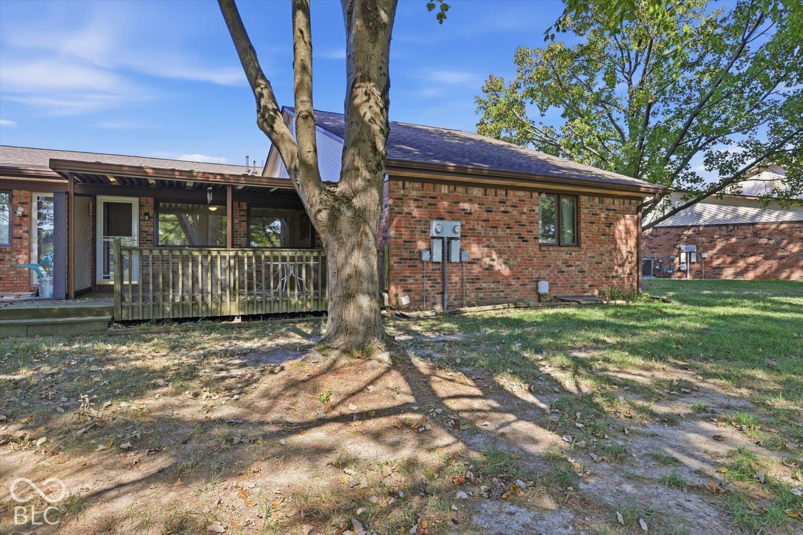 Brick exterior facade featuring a covered wood deck and mature landscaping