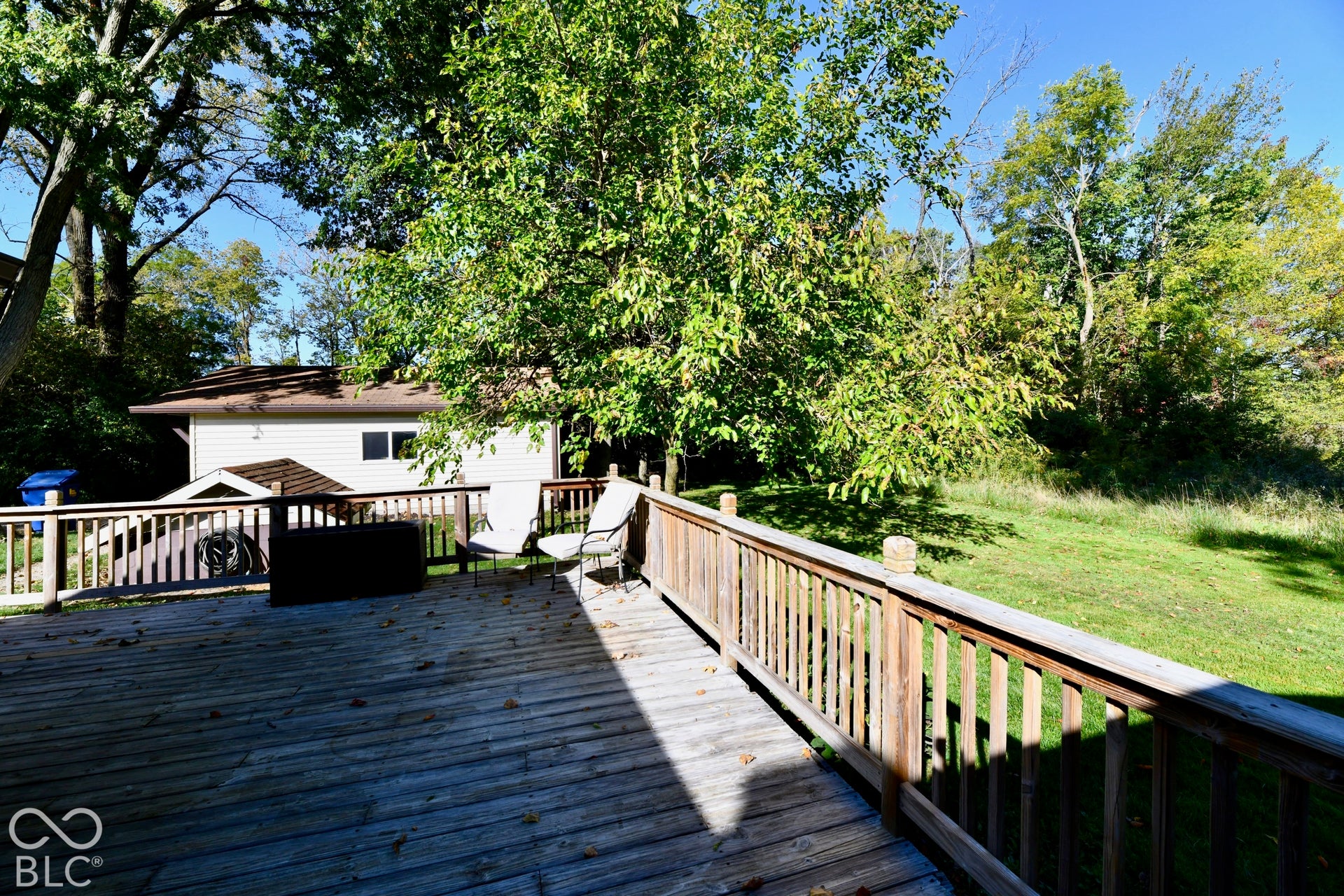 Wood deck with wood railing, leading to a grass area surrounded by mature trees