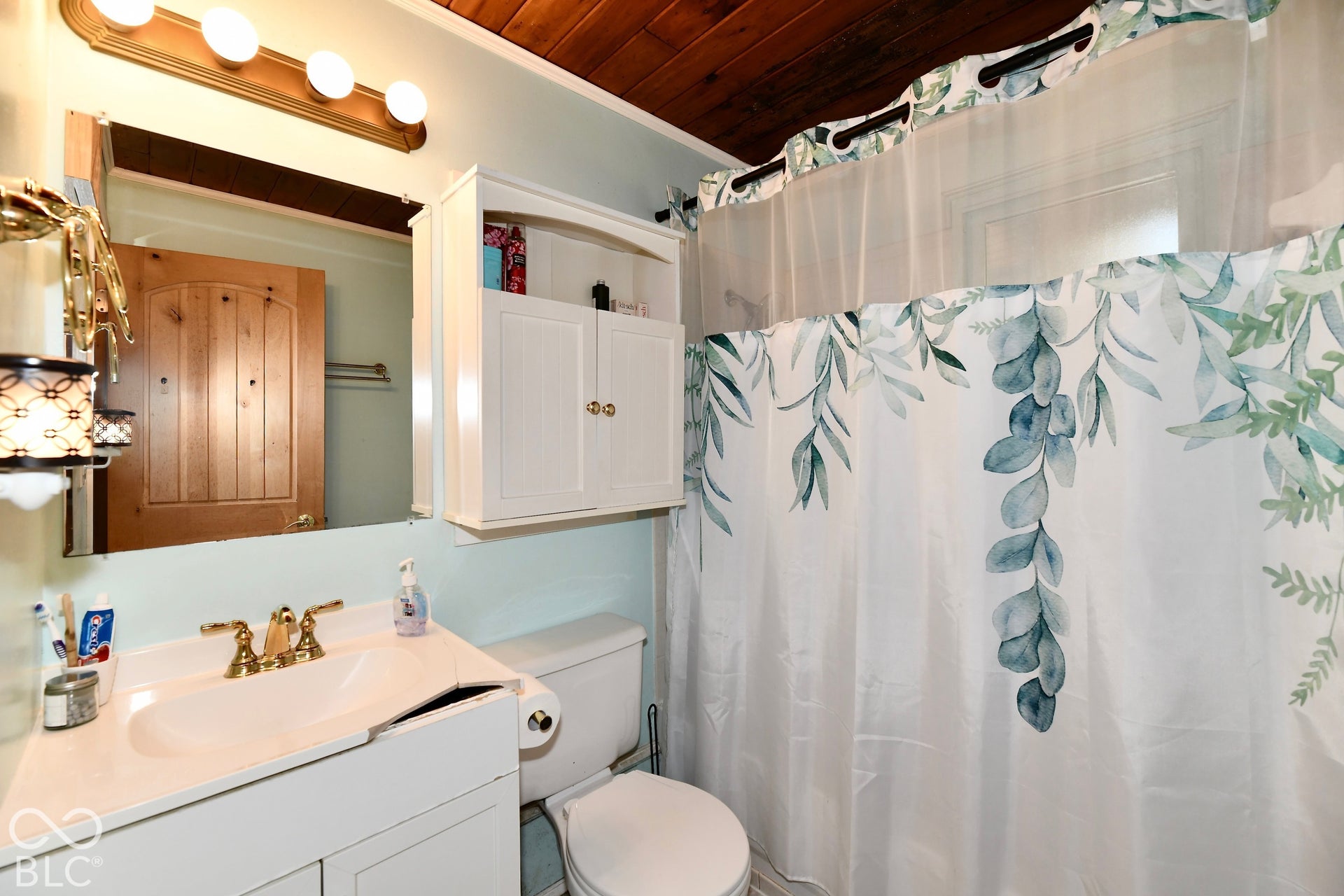 White vanity with integrated sink, brass-finish faucet, and a wall-mounted mirror