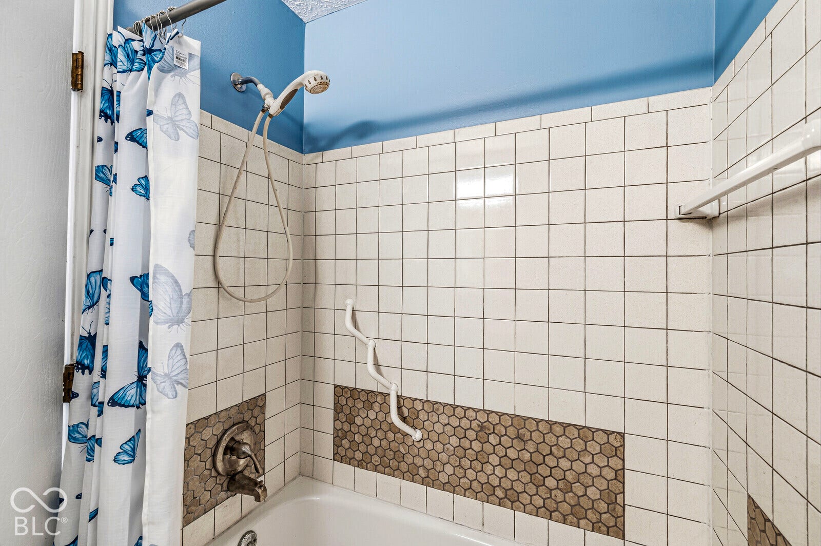 Tub and shower combination featuring white square tile surround, hexagonal accent tile, and a handheld shower head