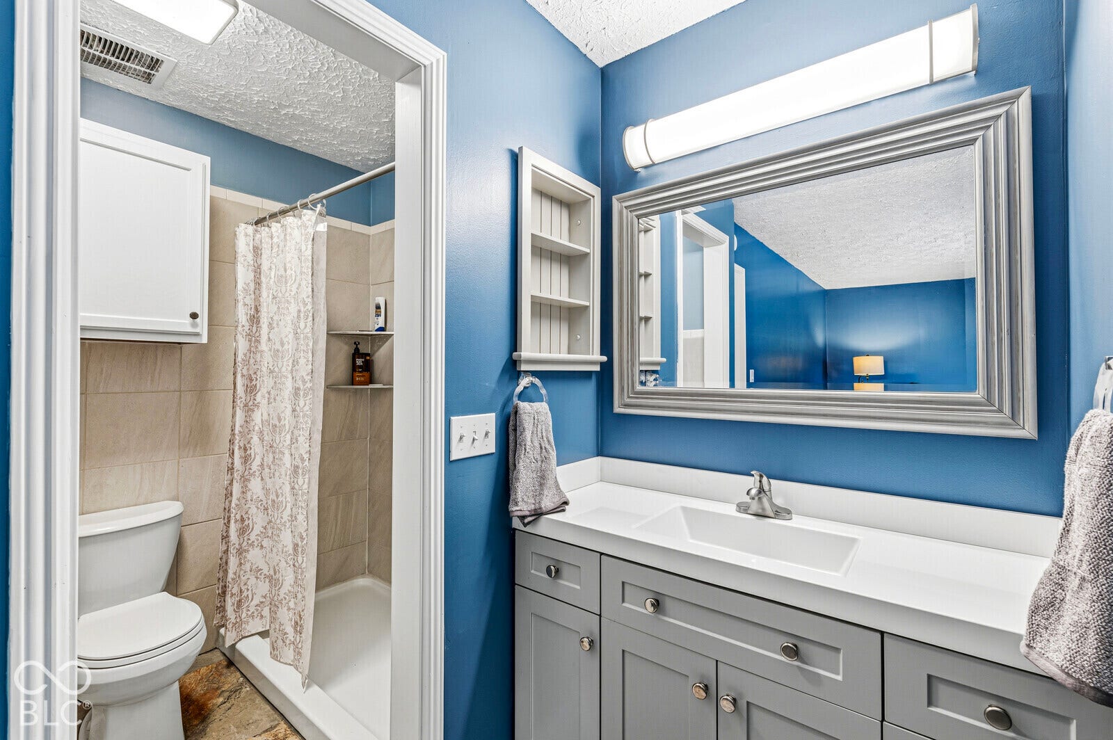 Vanity with integrated sink, framed mirror, wall-mounted light fixture, and walk-in shower with tile surround