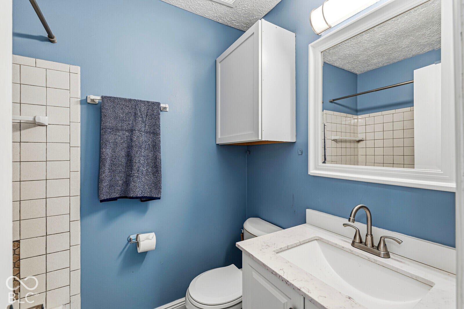 Vanity with a white countertop and integrated sink, brushed nickel faucet, wall-mounted cabinet, and large framed mirror