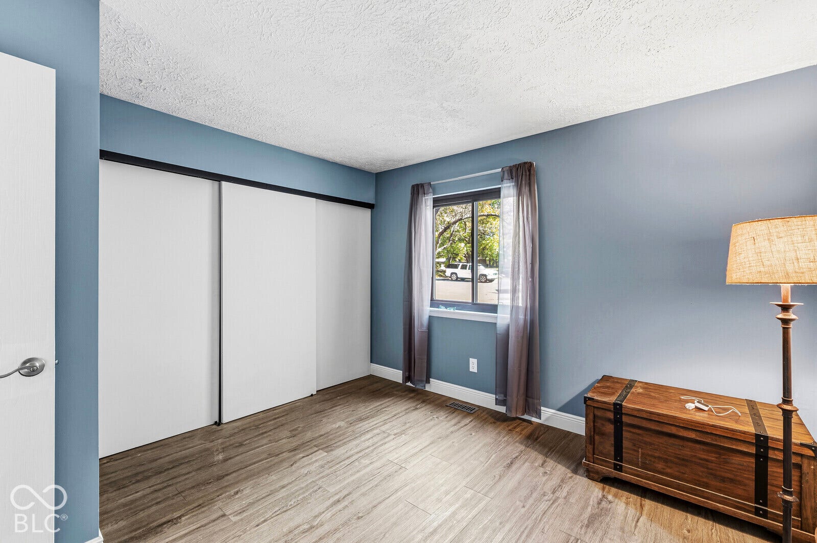 Wood-finish flooring, sliding closet doors, window with natural light, blue painted walls, and textured white ceiling