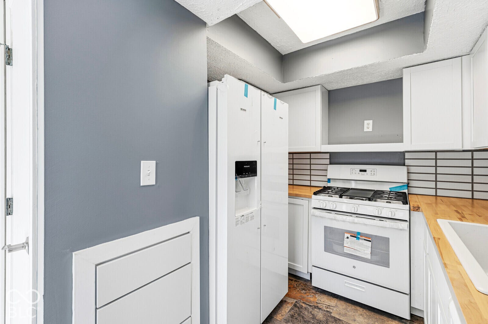 White cabinetry, wood-finish countertops, subway tile backsplash, white gas range, and a white refrigerator with water/ice dispenser
