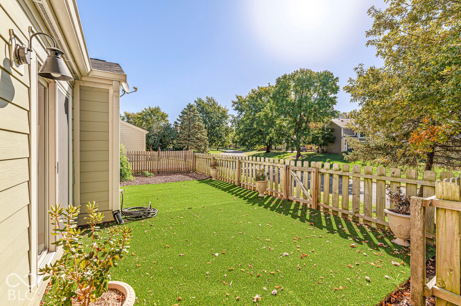 Fenced outdoor area featuring green ground covering and mature trees