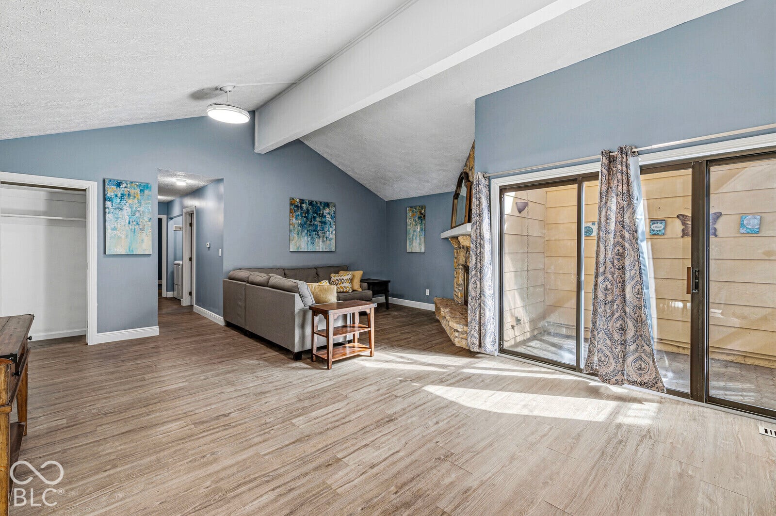Vaulted ceiling with exposed beam, wood-finish flooring, stone fireplace, and sliding glass doors