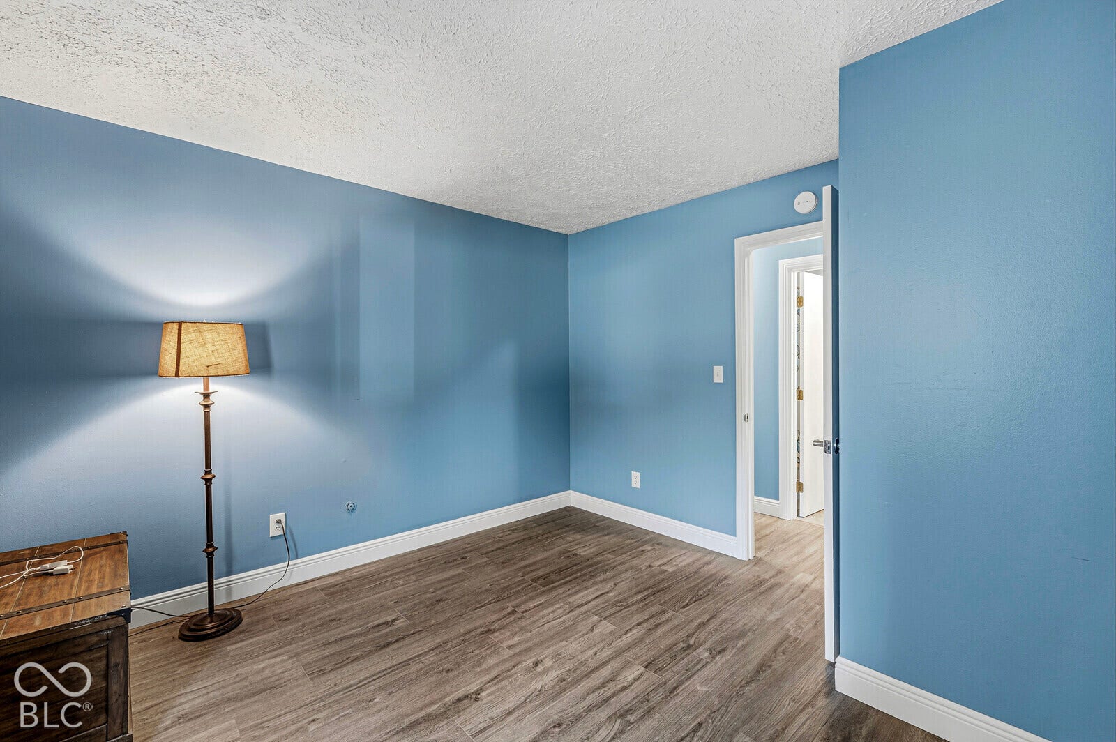 Wood-finish flooring with white trim, blue painted walls, and textured white ceilings