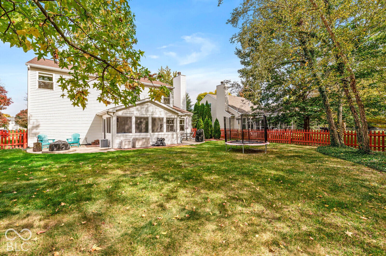 Spacious backyard featuring a large grass lawn, enclosed sunroom, concrete patio, and decorative wood fencing with mature trees
