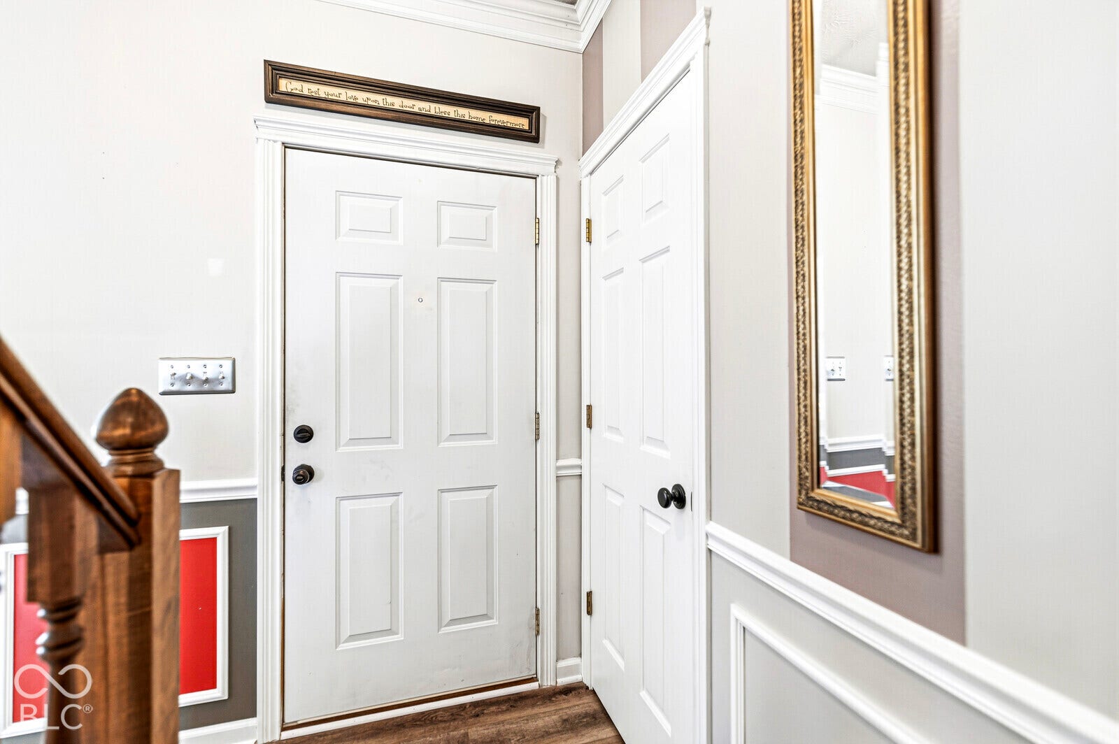 Entryway featuring a multi-panel door with matte black hardware, wainscoting detail, wood-finish flooring, and a wooden staircase railing with a decorative newel post