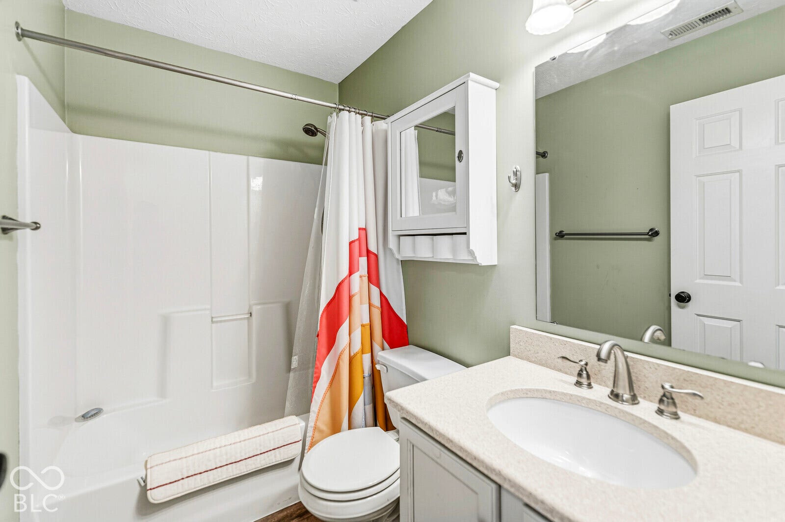 Bathroom featuring a vanity with a light-toned solid surface countertop, undermount sink, brushed nickel faucet, wall-mounted medicine cabinet, and a shower-tub combination with a white surround