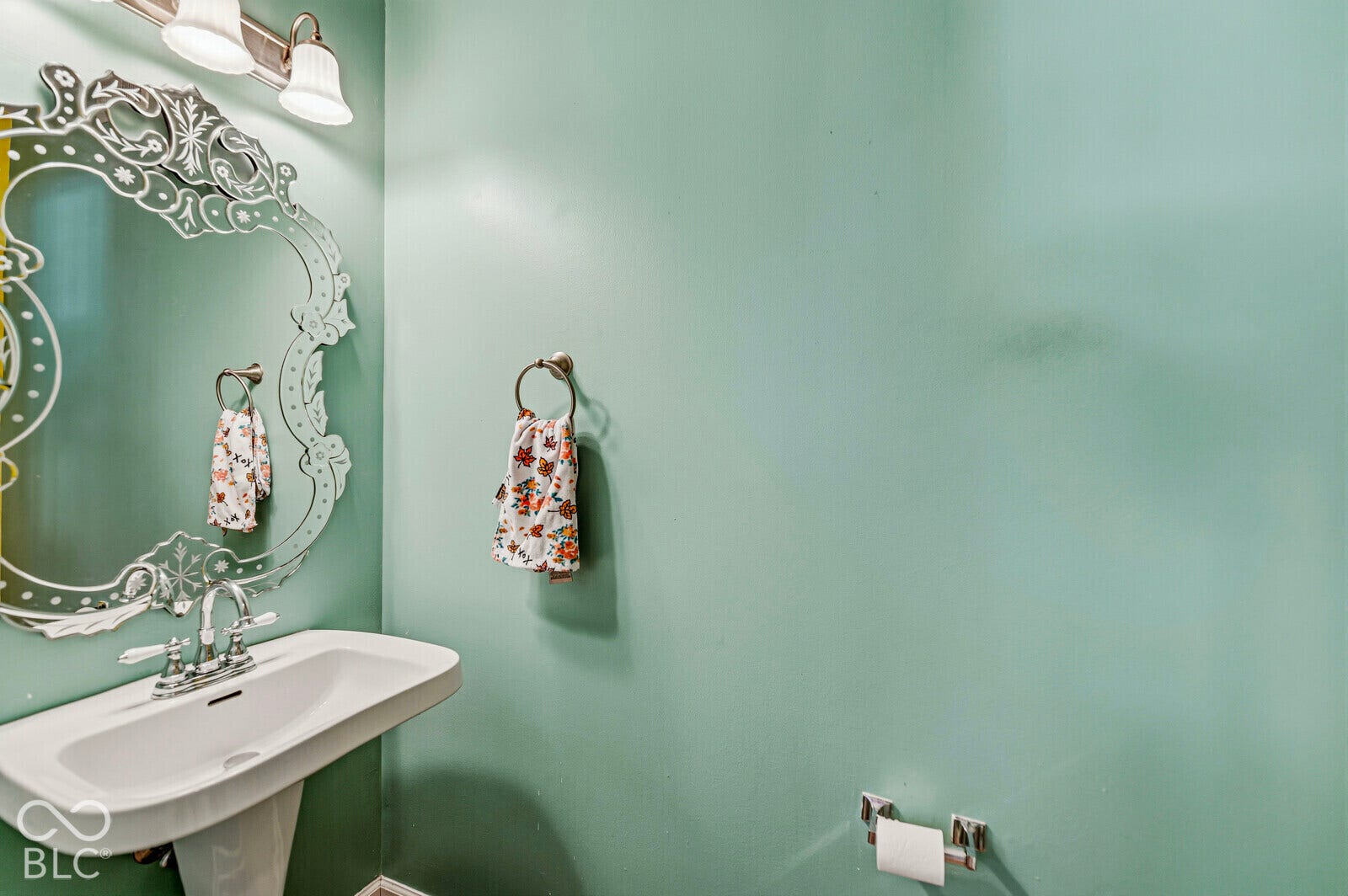 Pedestal sink featuring a polished chrome widespread faucet, decorative wall-mounted mirror, and matching light fixture with three glass shades