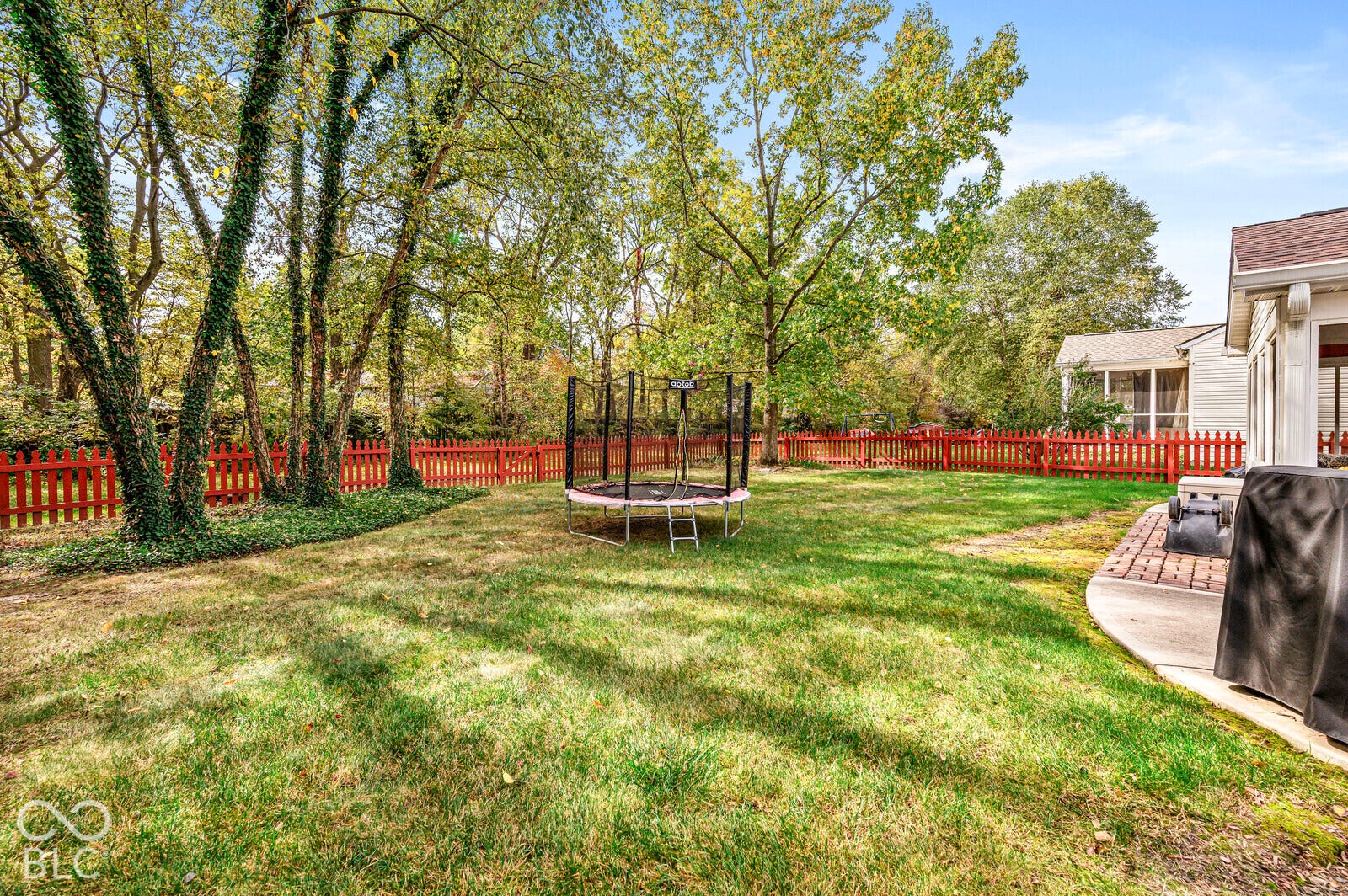 Private backyard featuring a fenced perimeter, expansive lawn area, brick-paved patio, and mature tree canopy