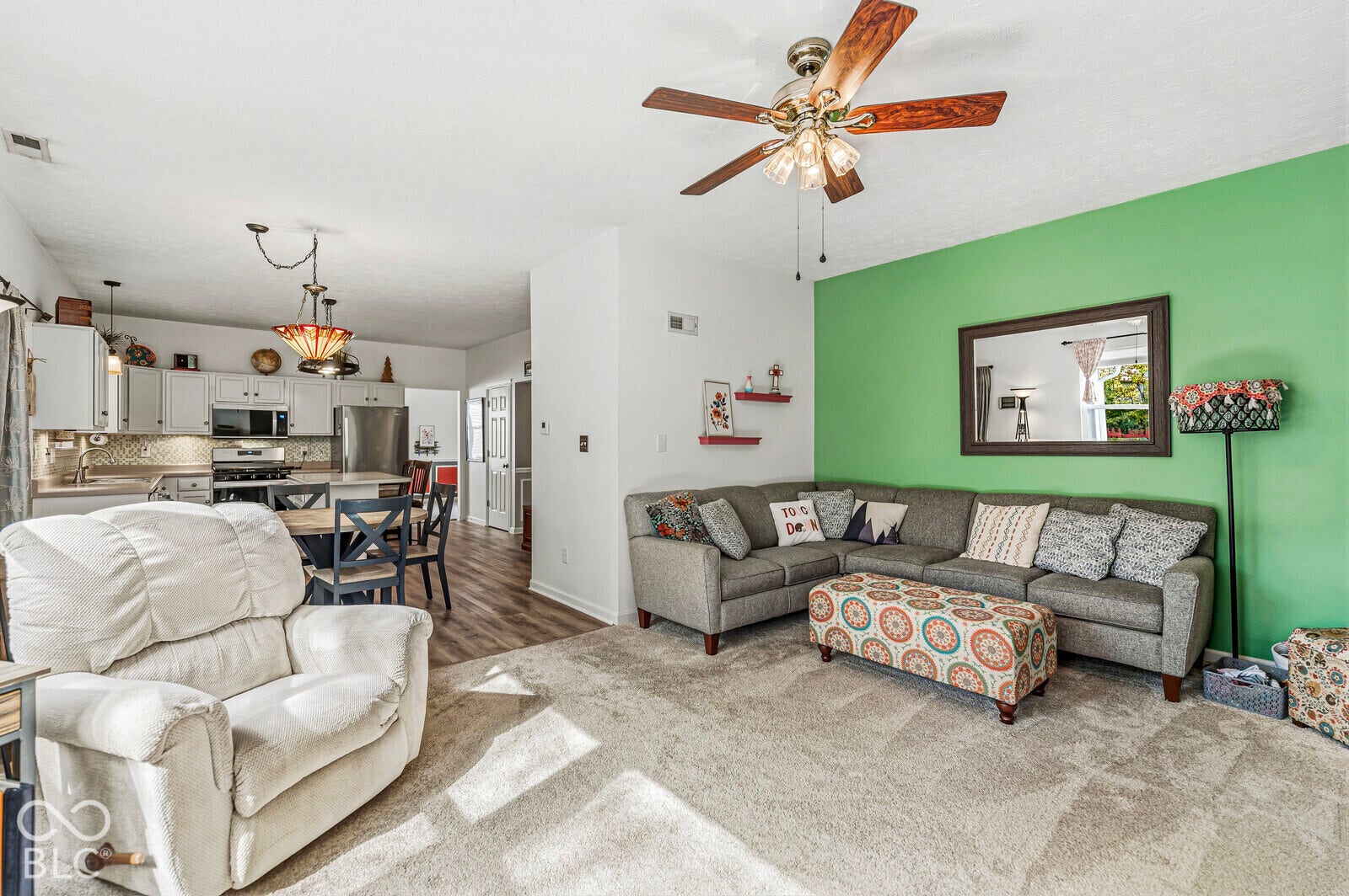 Open-concept interior featuring wood-finish flooring, a ceiling fan with integrated lighting, and kitchen cabinetry with stainless steel appliances
