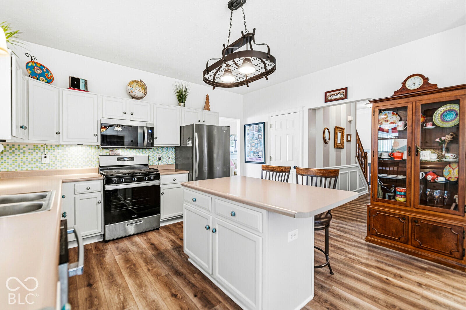 Kitchen featuring white cabinetry, wood-finish flooring, a central island, mosaic-tile backsplash, and stainless-steel appliances