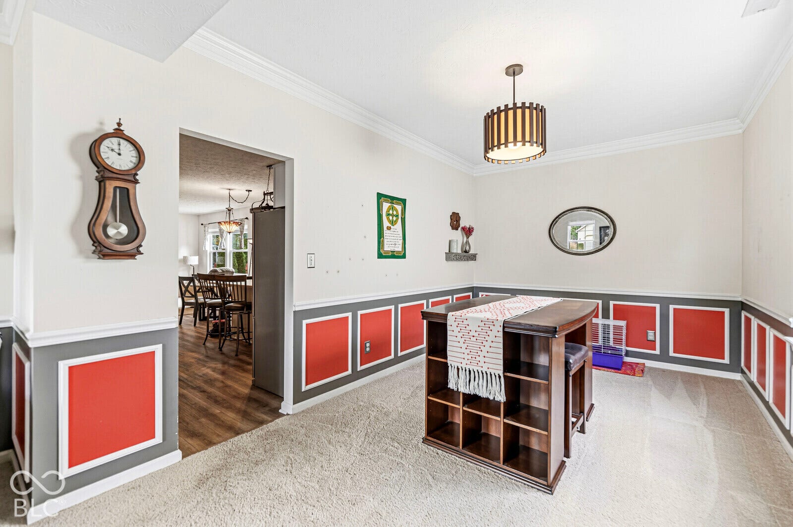 Dining area featuring decorative wainscoting with accent panels, crown molding, a central drum pendant light fixture, and neutral carpeting