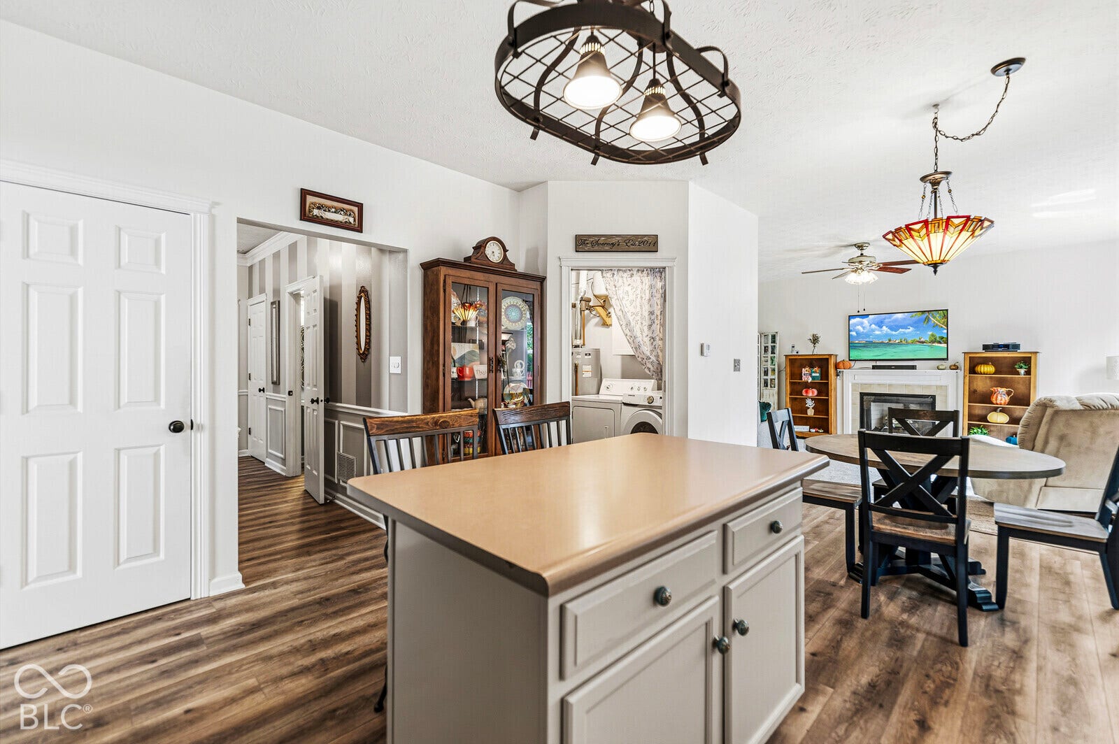 Kitchen island with neutral cabinetry and solid surface countertop, wood-finish flooring, and industrial-style metal cage pendant lighting