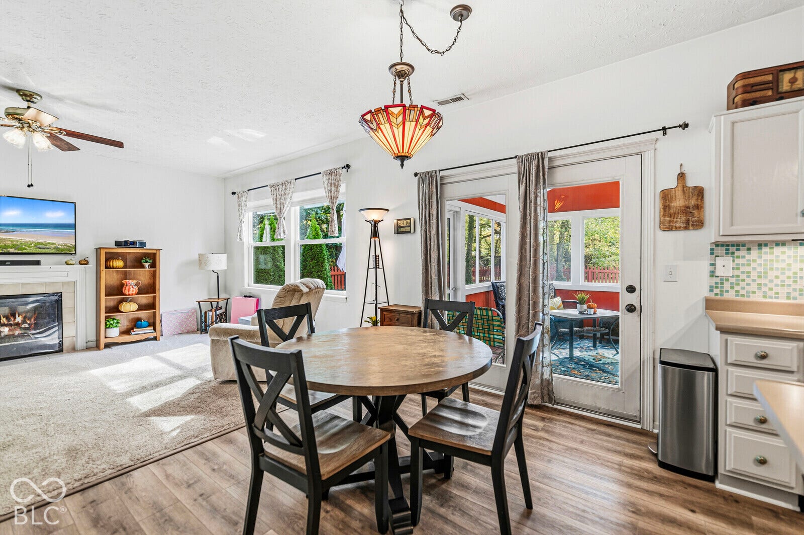 Living area featuring a gas fireplace with a stone-surround mantel, wood-finish flooring, decorative multi-tiered pendant light, and glass-paned doors opening to an enclosed porch
