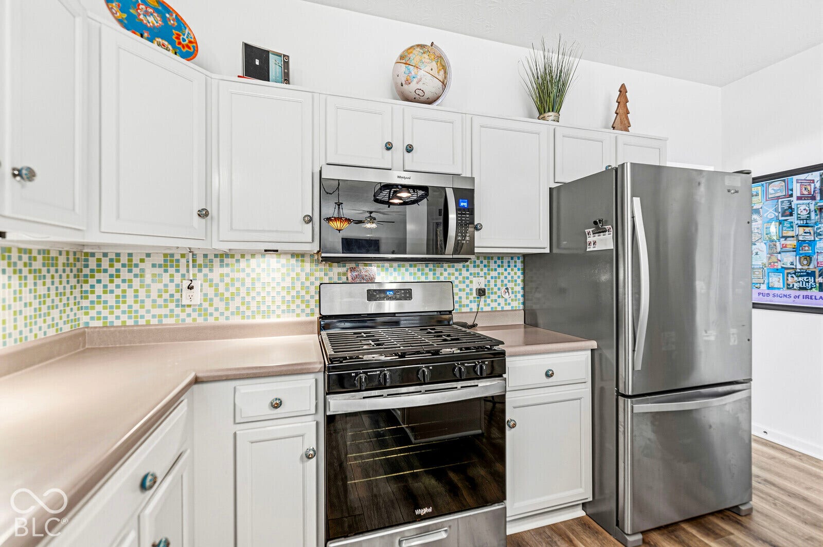 Kitchen featuring white shaker-style cabinetry, stainless steel appliances, a multi-colored mosaic tile backsplash, and wood-finish flooring