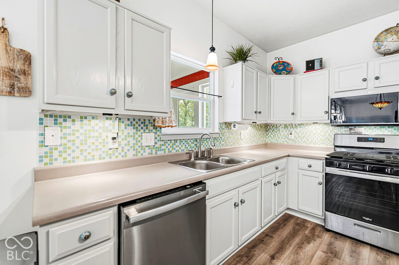 Kitchen featuring white cabinetry, solid-surface countertops, a multicolored mosaic tile backsplash, stainless steel appliances, and wood-finish flooring