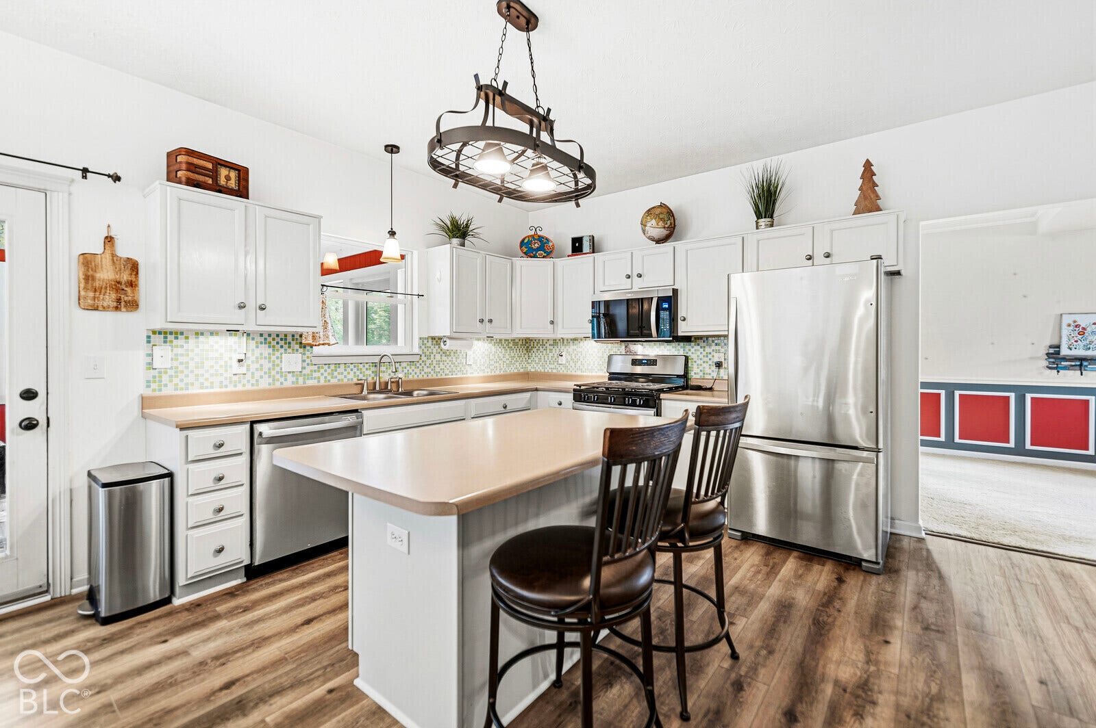 Kitchen featuring white cabinetry, wood-finish flooring, a central island, stainless steel appliances, and a mosaic tile backsplash
