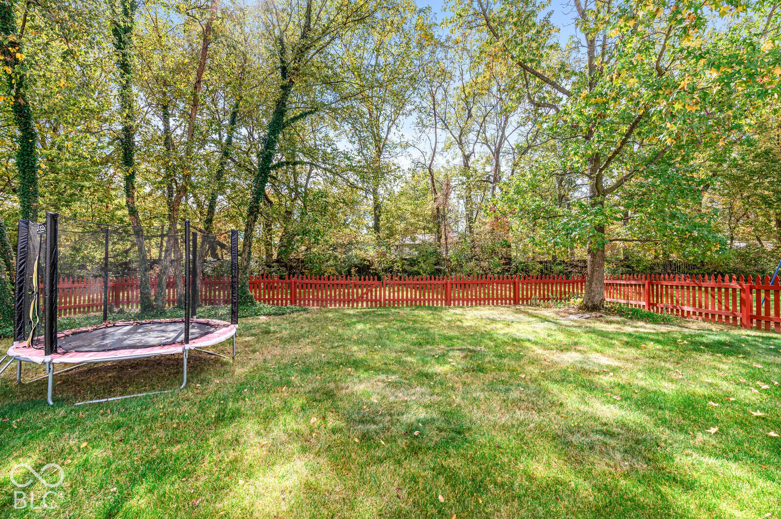 Backyard featuring a grass lawn, red picket fencing, and mature trees