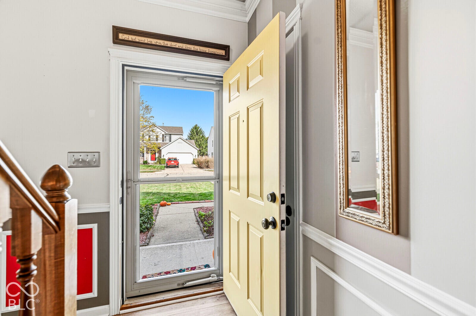 Entryway featuring a solid panel front door, white crown molding, custom wall trim detailing, and a wood-finish staircase banister