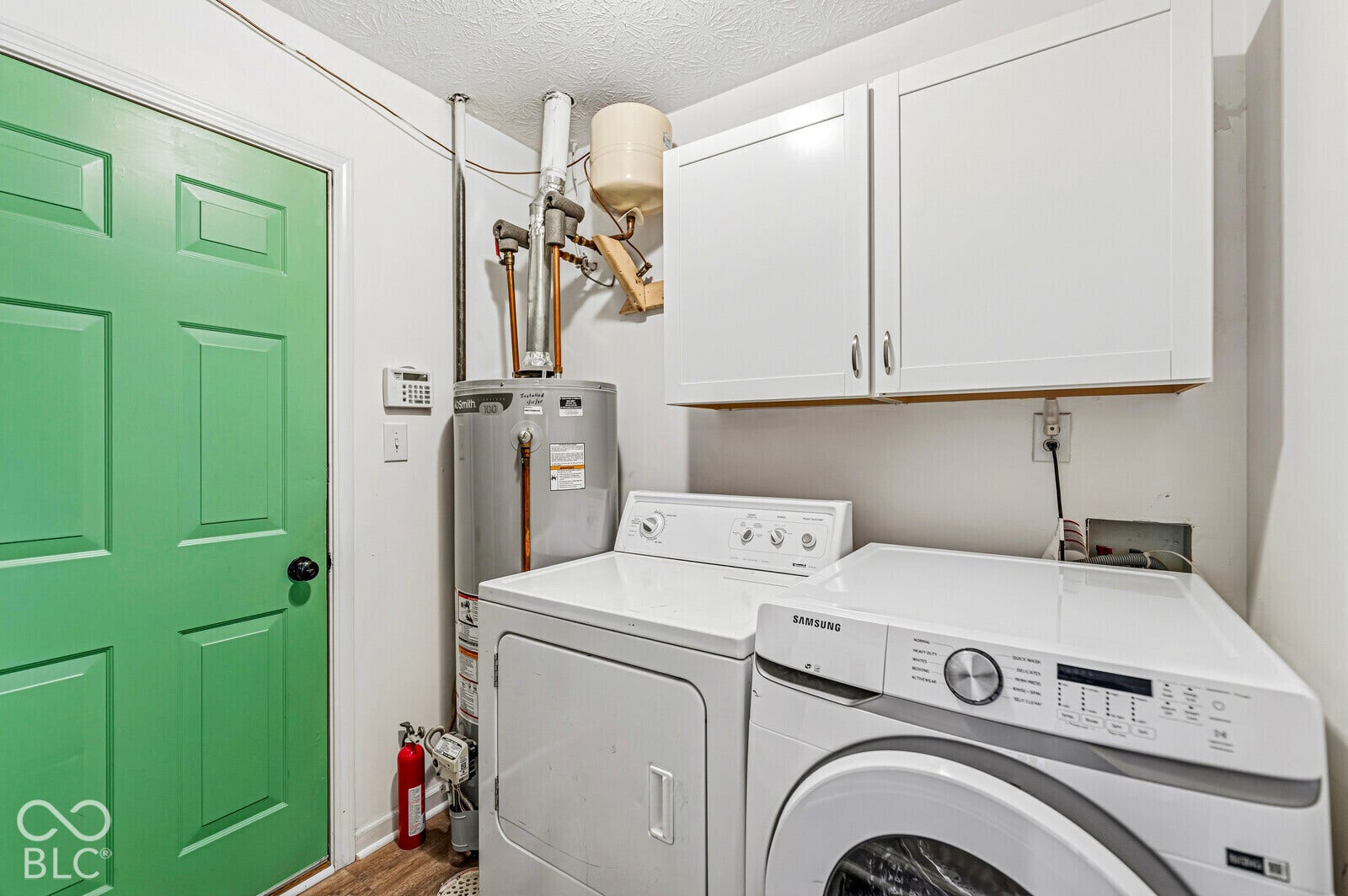 Utility room featuring white wall-mounted upper cabinetry, a green paneled door, and a dedicated area for laundry equipment