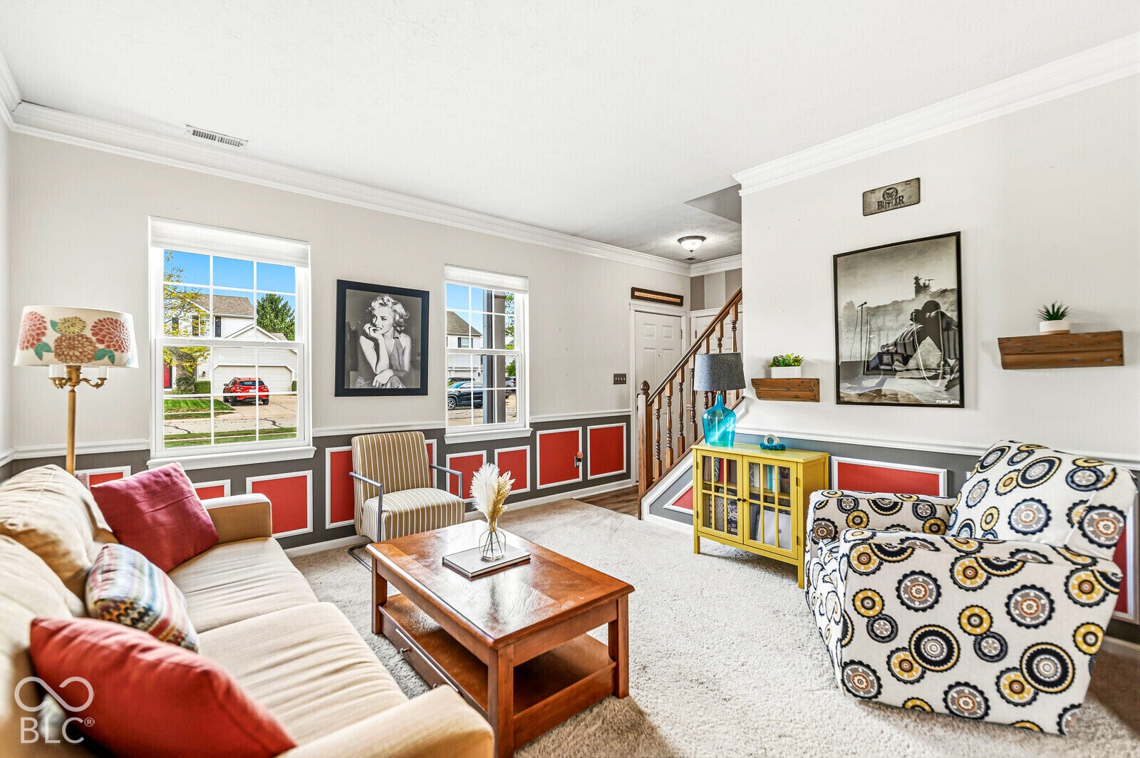 Living area featuring decorative wall paneling, crown molding, double-hung windows, and a wooden staircase handrail