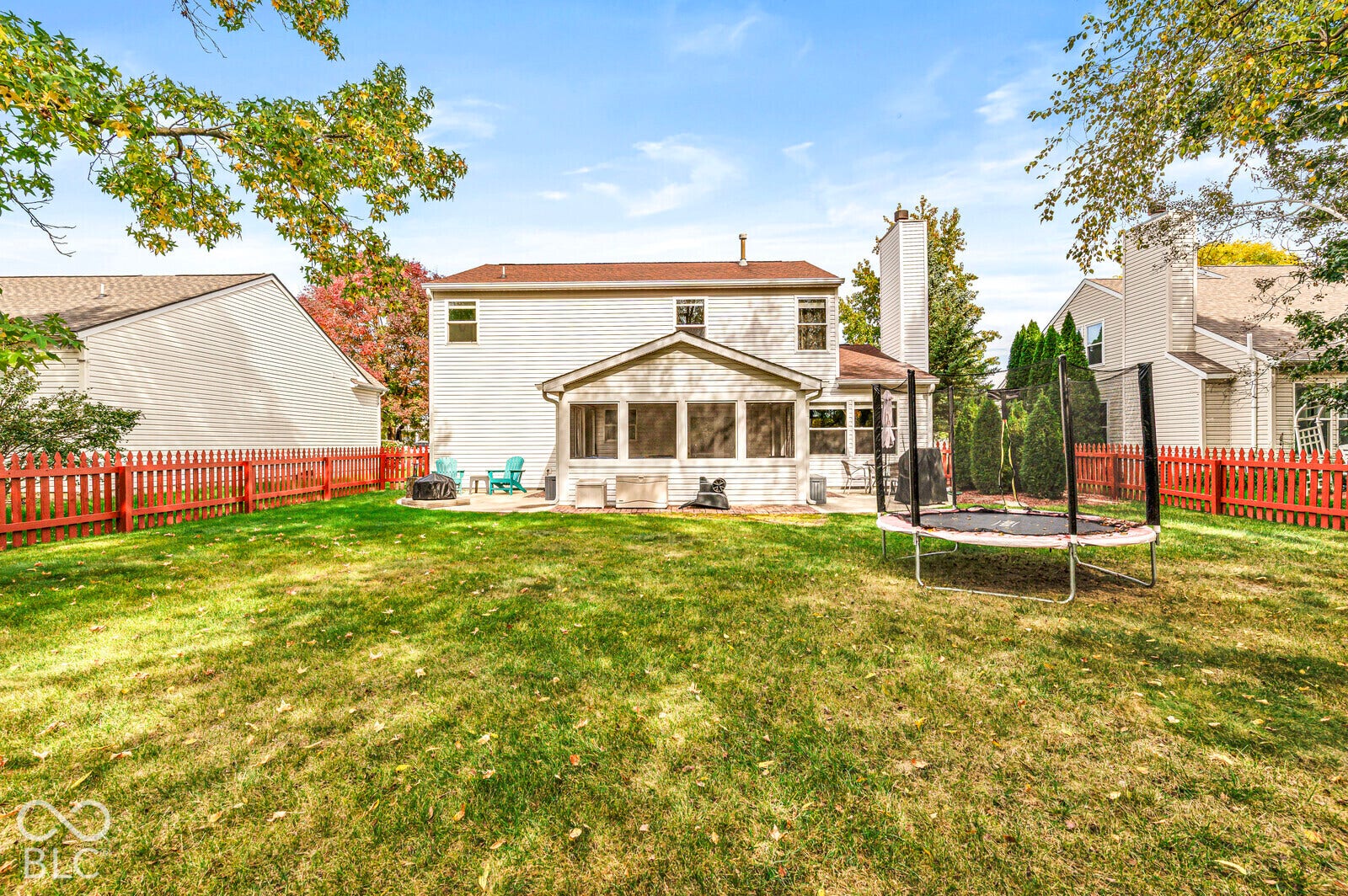 Rear exterior featuring a screened porch, concrete patio, full-height chimney, and perimeter wood fencing surrounding a grass lawn