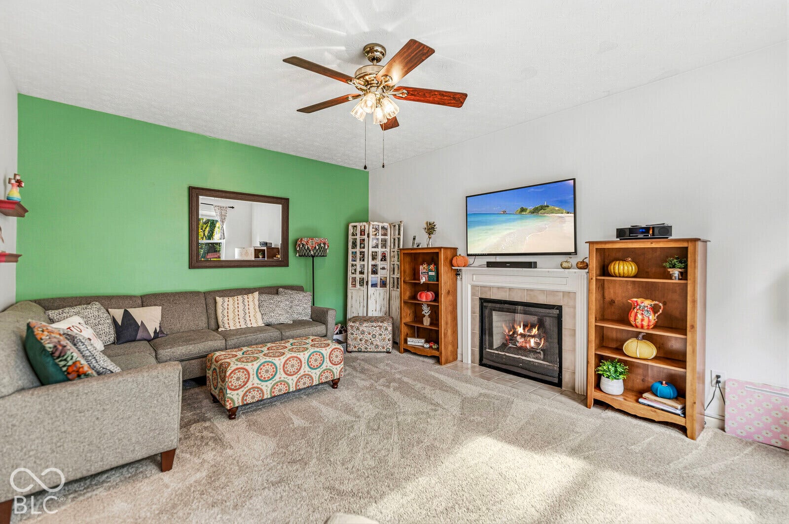 Fireplace with a stone-finish surround and mantel, ceiling fan with integrated lighting, and neutral carpeting